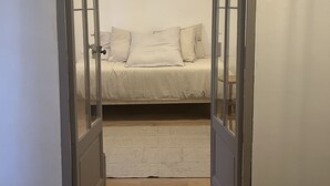 Une pièce avec un lit, un petit tapis et une porte qui donne sur une autre pièce.