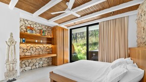 Ein Schlafzimmer mit Steinwand, Holzregalen, einem Bett und Blick auf Grünflächen.