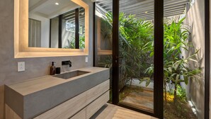 Ein modernes Badezimmer mit einem großen Spiegel, zwei Waschbecken und Gartenblick durch eine Glastür.