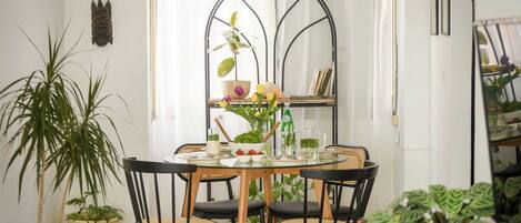 A dining area with a round table, black chairs, and a black metal shelf with plants.