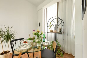 A dining area with a glass table, chairs, potted plants, and a metal shelf unit.