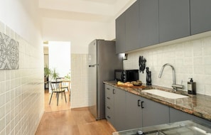 A modern kitchen with grey cabinets, a stainless steel refrigerator, a granite countertop, and a sink.
