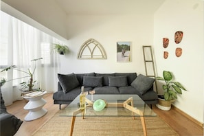 A modern living room with a glass coffee table, a dark grey sofa, and a large window with sheer curtains.