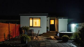 Una casa moderna amb façana blanca, una tanca de fusta, un patio amb taula i cadires, i una banyera hidromassatge.