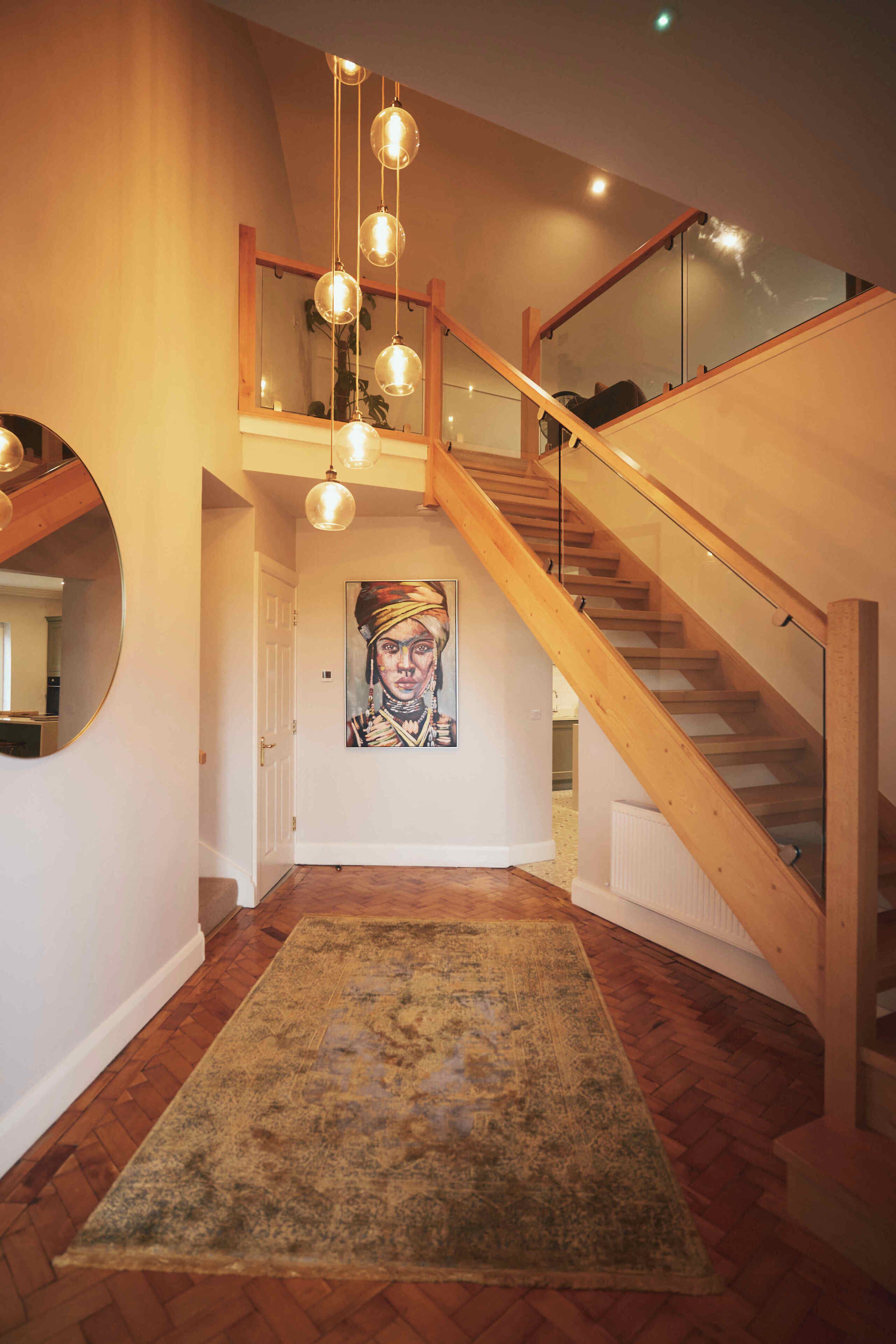 Un escalier avec des rampes en bois et des panneaux de verre, menant à l’étage supérieur. Un tableau est visible sur le mur situé en contrebas de l’escalier.