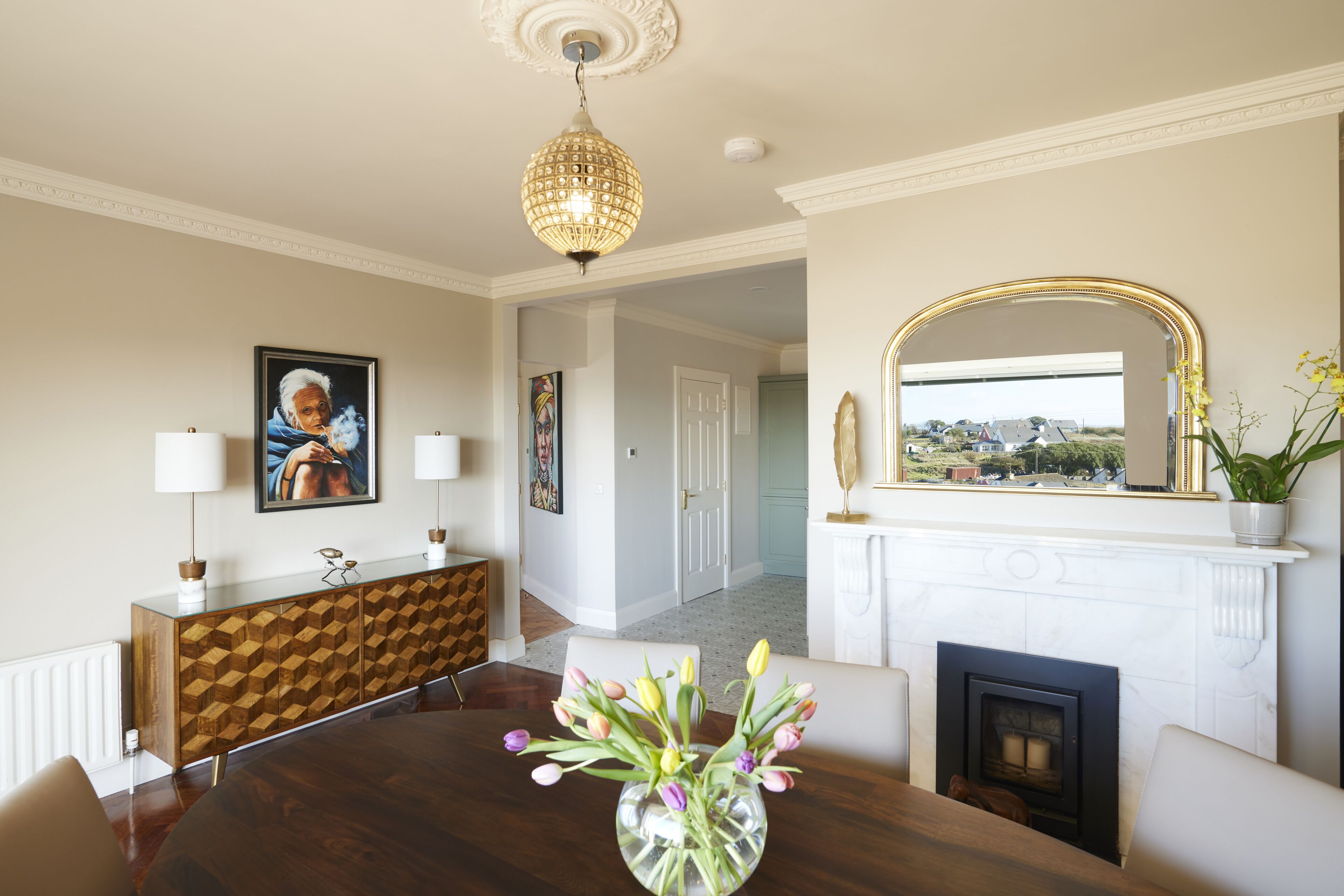 A dining room with a round table, a vase of flowers, a wooden cabinet, and a fireplace.