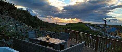 A stone wall, wicker furniture, and a view of the sea at sunset.