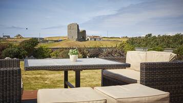 An outdoor patio with wicker furniture and a view of a historic stone tower in the distance.