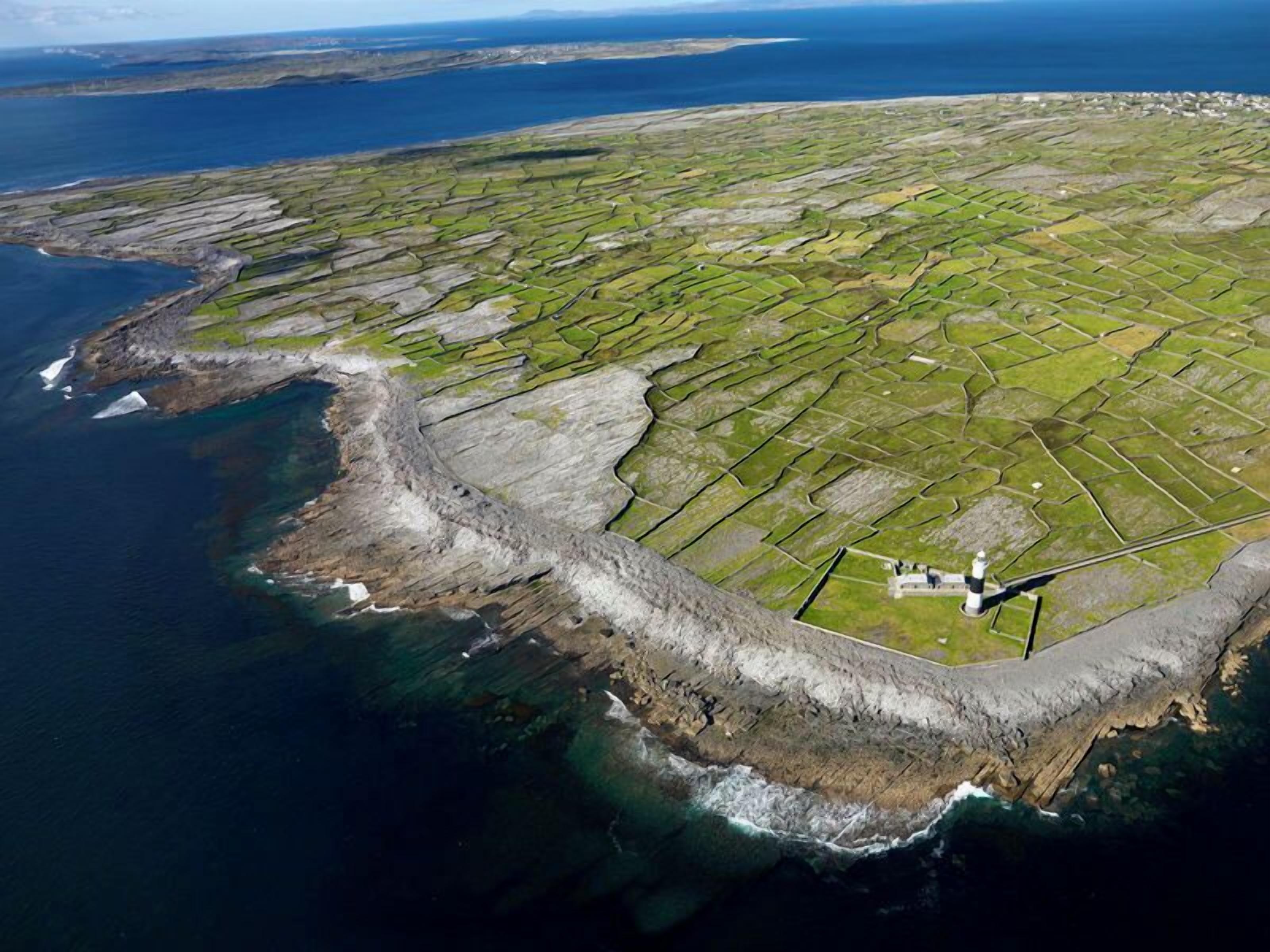 An aerial view of a coastal area with terraced fields and a lighthouse.