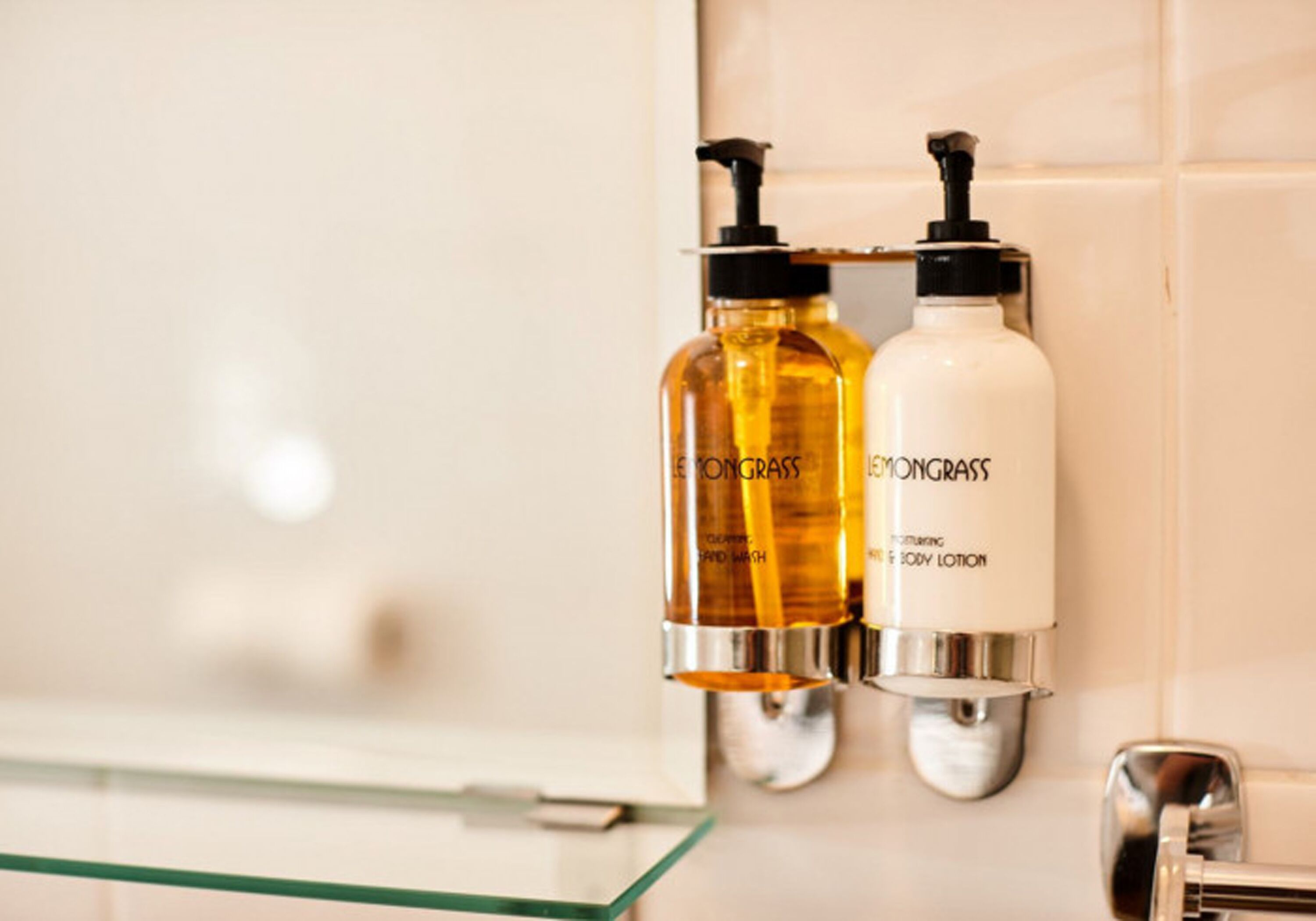 Dos botellas de loción corporal y jabón de ducha 'Lemongrass' sobre una pared de baño.