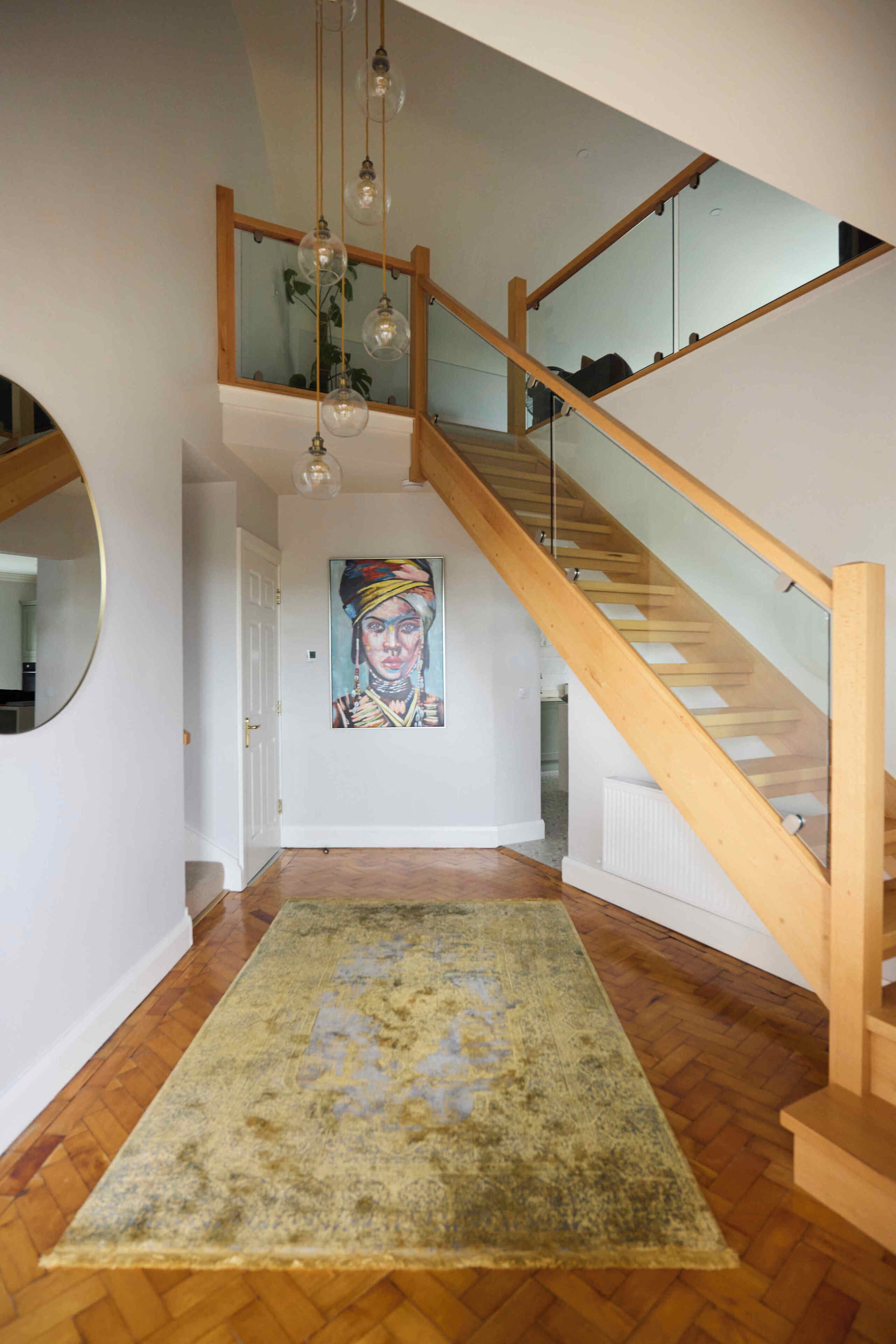 A staircase with wooden railings and glass panels, leading to an upper floor. A painting is visible on the wall above the staircase.