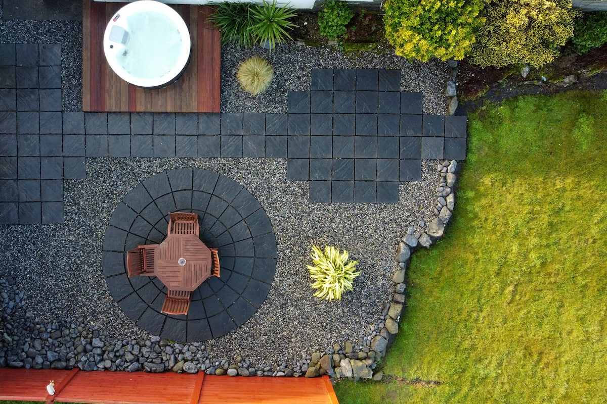 Eine Terrassenanlage mit rundem Tisch und Stühlen, umgeben von einer Steinmauer, und eine Whirlwanne im Hintergrund.