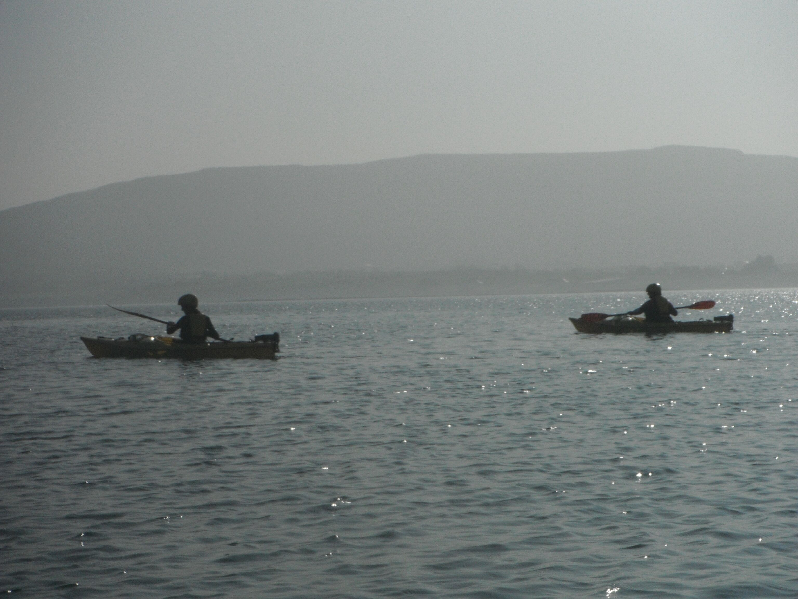 Two kayaks on a calm body of water with a hilly landscape in the background.
