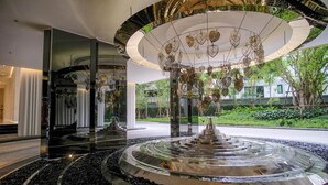 Une fontaine intérieure moderne, de forme circulaire, entourée d’un bassin réfléchissant et protégée par une enceinte en verre.