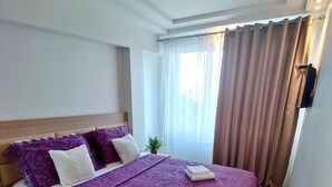 Een hotelkamer met een groot bed, een houten hoofdeinde, een kleine plant in een pot en een raam met gordijnen.