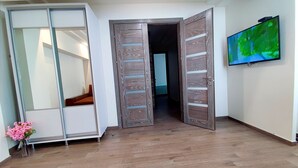 Een kamer met een houten vloer, een schuifdeur, een televisie aan de muur en een bloevas.