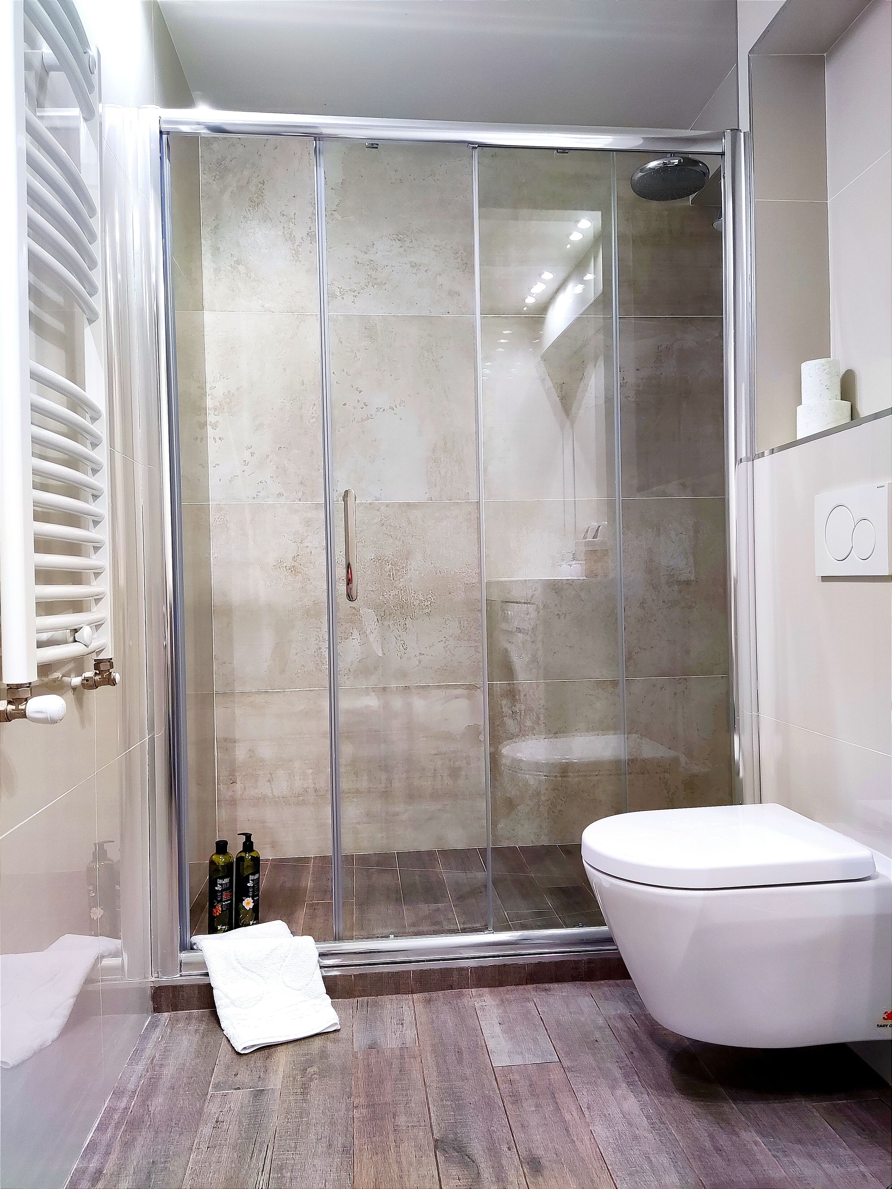 Ein modernes Badezimmer mit einer gläsernen Duschkabine, einer weißen Toilette und einem Holzboden.