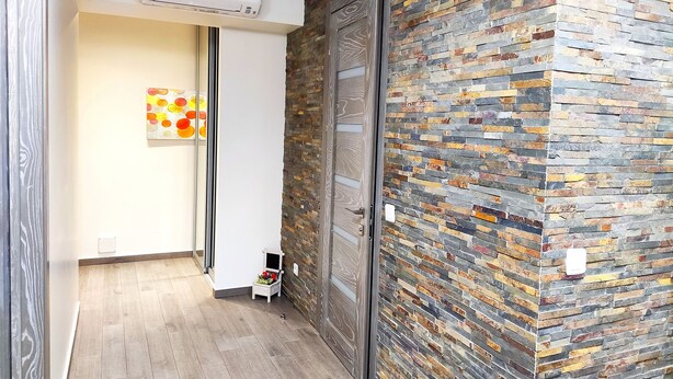 Een hal met een houten vloer, een moderne airconditioning, een decoratieve wand met een mozaïekpatroon, en een deur met een ruitpaneel.