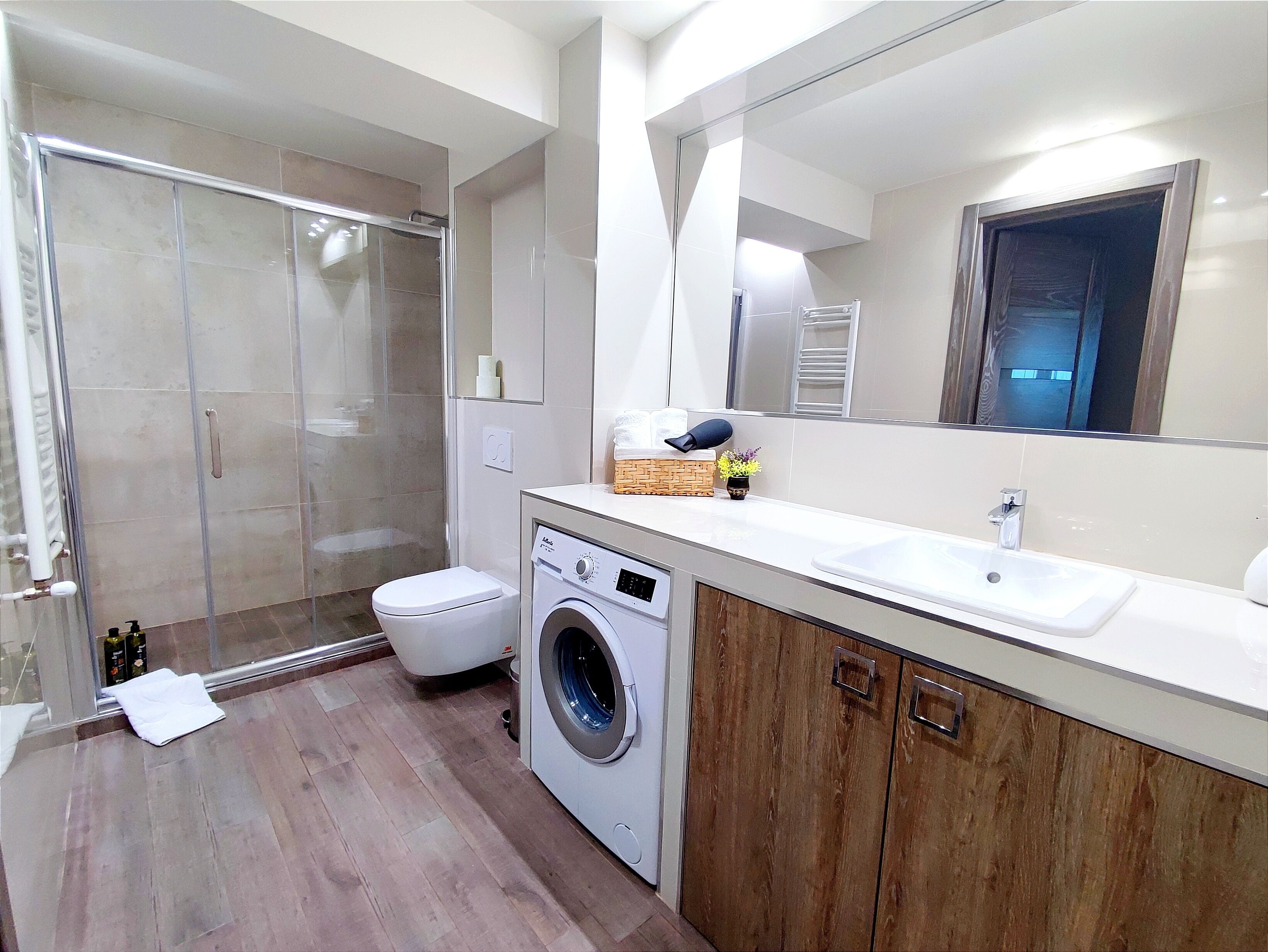 A modern bathroom with a glass shower enclosure, a built-in washing machine, and a large mirror.