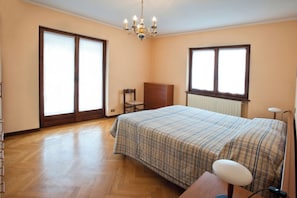 Un dormitorio con cama, una silla, un escritorio, una lámpara, un radiador y una ventana.