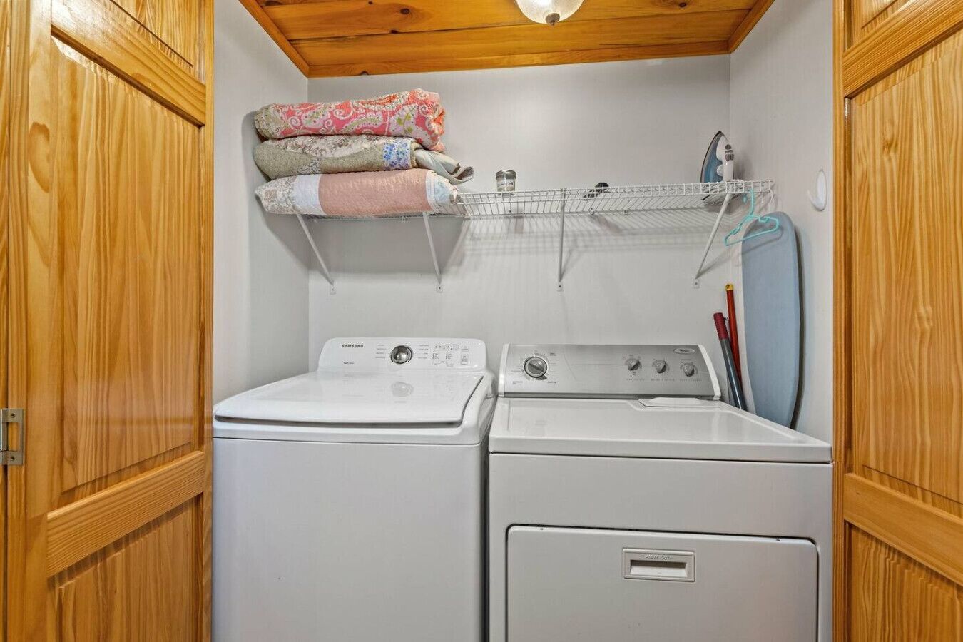 Un cuarto de lavandería con dos lavadoras, un tendedero y estantes con ropa doblada.