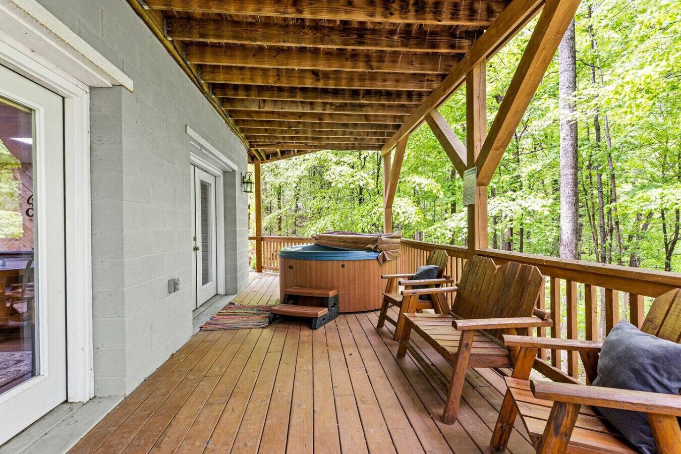 A wooden deck with a hot tub, chairs, and a view of a forest.