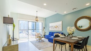 A modern living room with a dining area, large windows, a blue sofa, and a dining table set for four. - Downtown Charming Condo Close to Dubai Mall (Dubai)