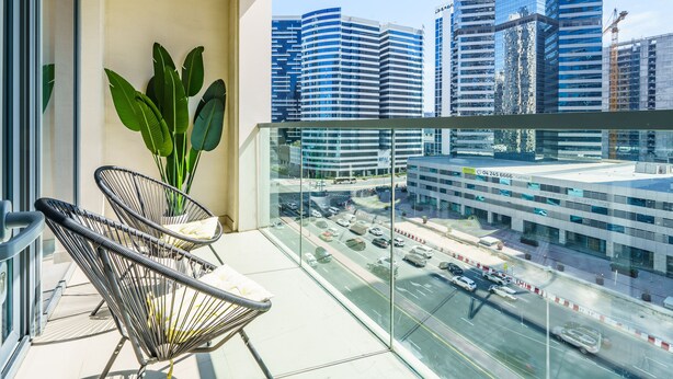 A balcony with two chairs, a potted plant, and a view of a cityscape with modern buildings. - Downtown Charming Condo Close to Dubai Mall (Dubai)
