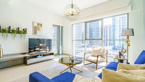 A modern living room with a large TV, comfortable seating, a coffee table, and a view of the city through large windows. - Downtown Charming Condo Close to Dubai Mall (Dubai)