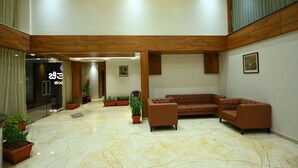 A spacious lobby with a marble floor, a brown leather sofa, and potted plants. - Chithara Comforts (Udupi)