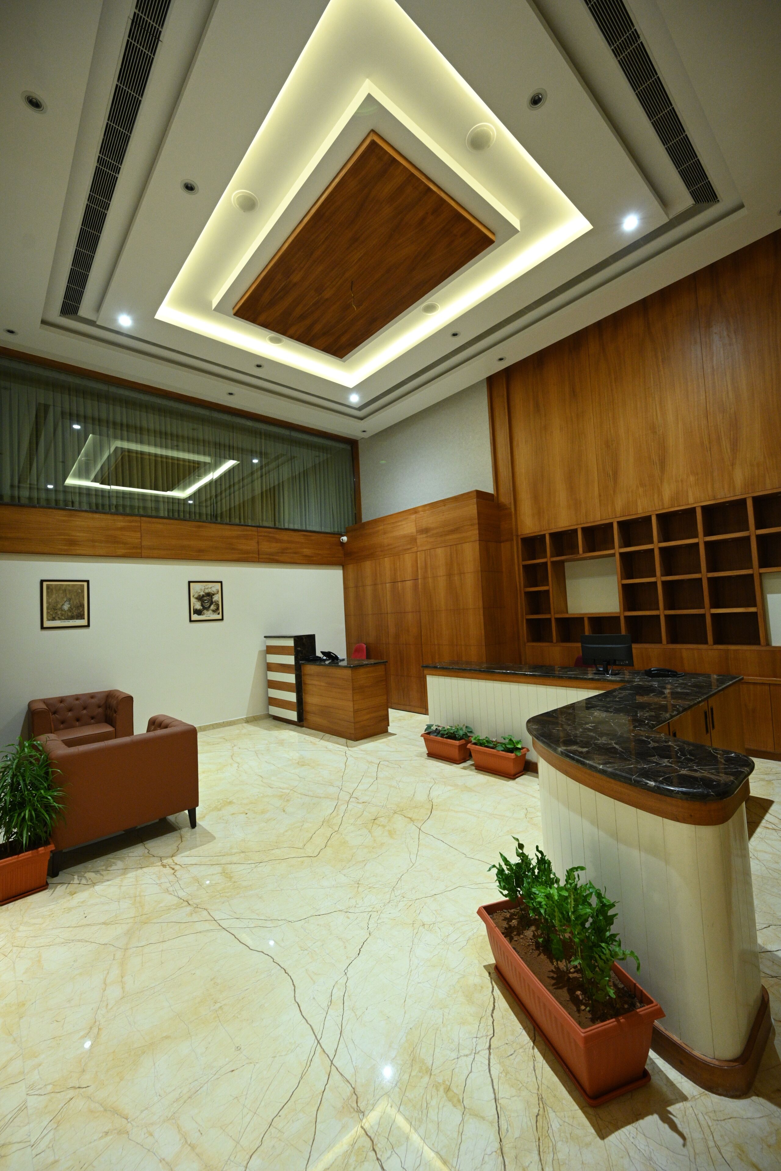 A modern lobby with a reception desk, seating area, and potted plants.