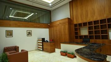 A modern lobby with a reception desk, seating area, and potted plants.