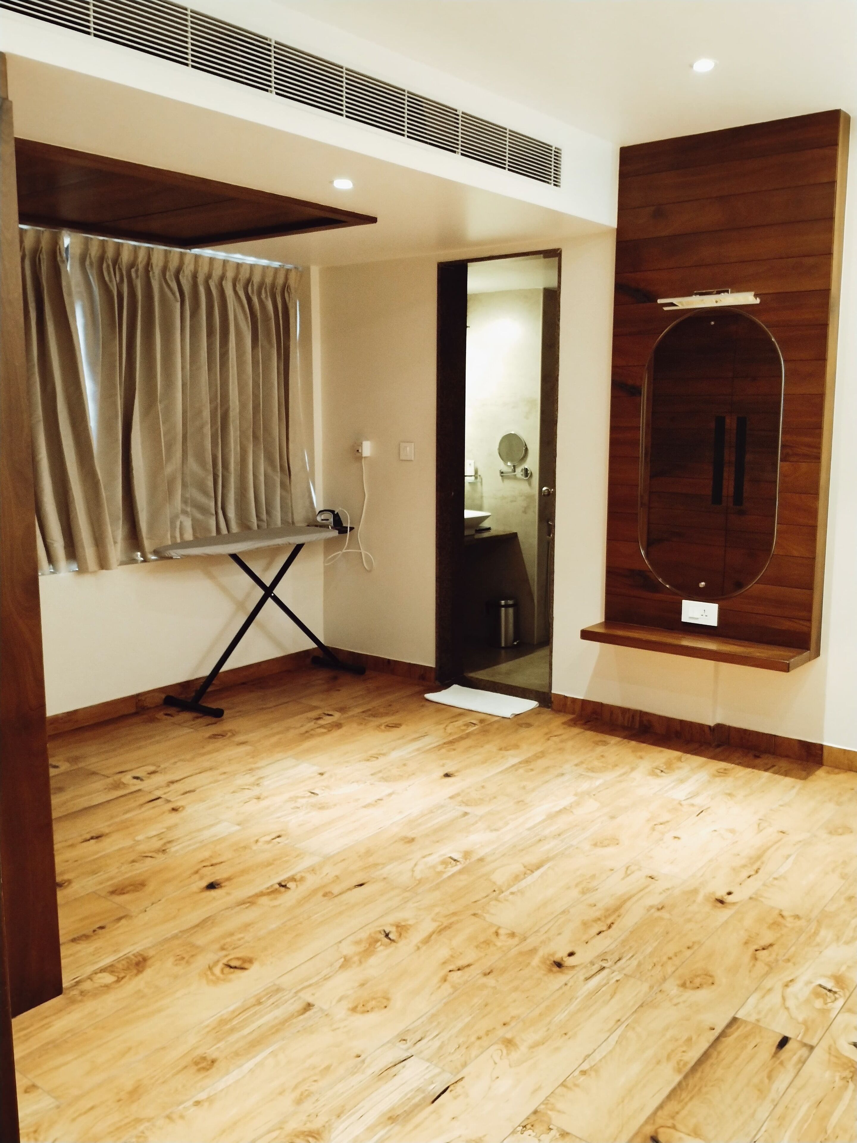 A room with wooden flooring, a mirror, a curtain, and a vent.