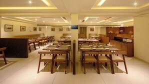 A hotel dining area with multiple tables and chairs, a reception desk, and a kitchen area. - Chithara Comforts (Udupi)
