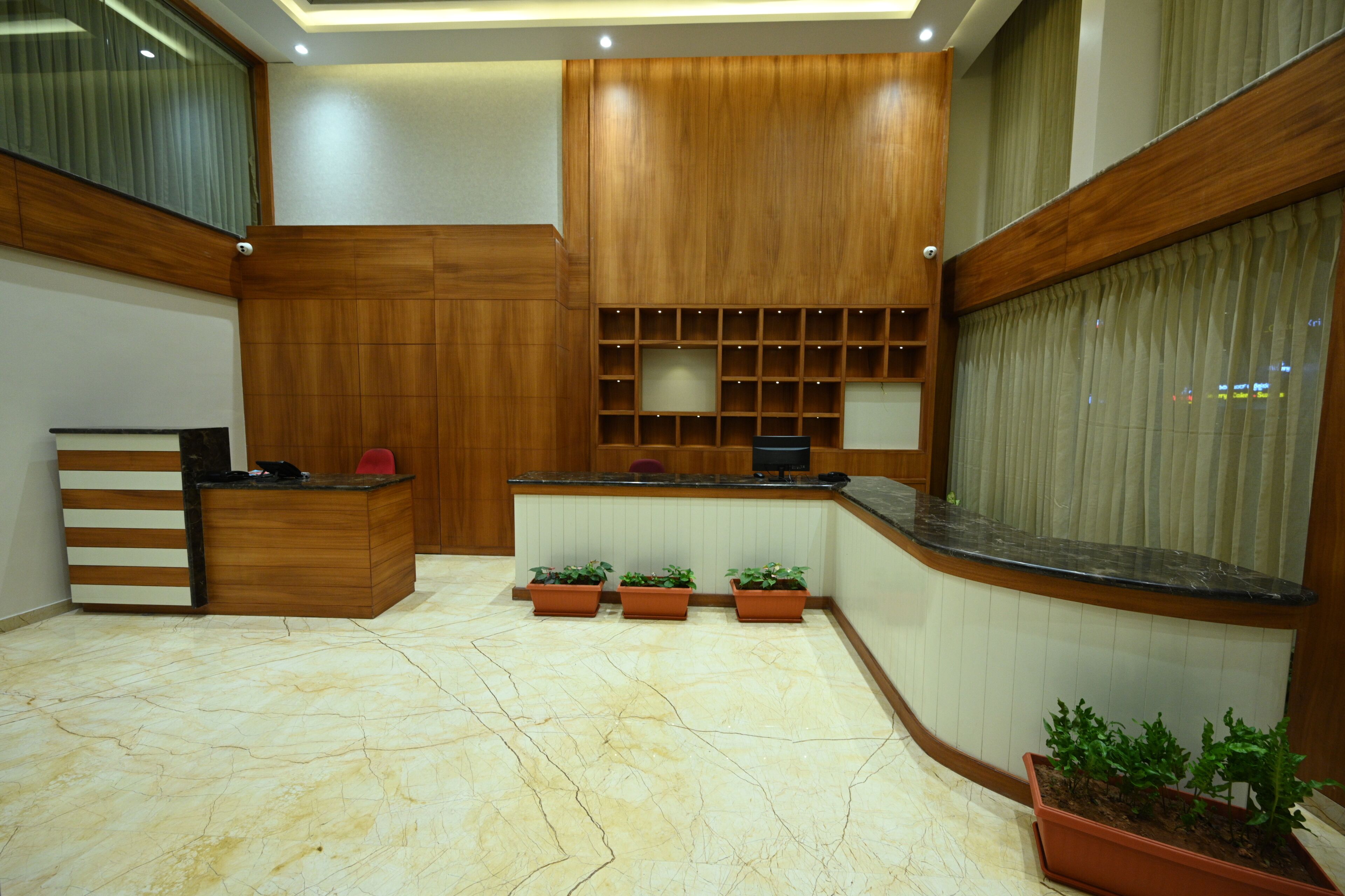 Un área de recepción con un mostrador de madera, plantas en macetas y un amplio ventanal con cortinas.
