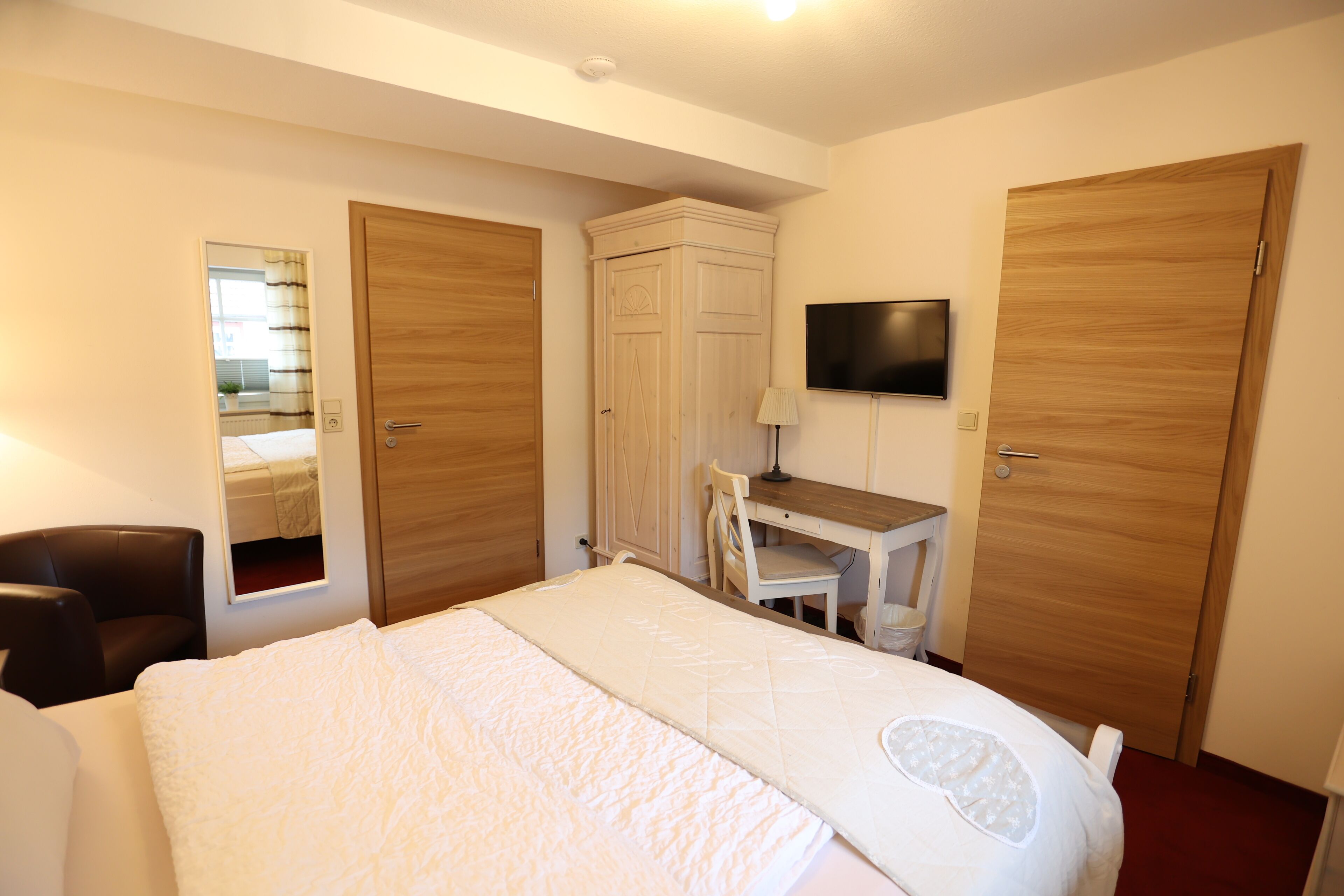 A hotel room with a bed, a desk, a chair, a TV, and two wardrobes.