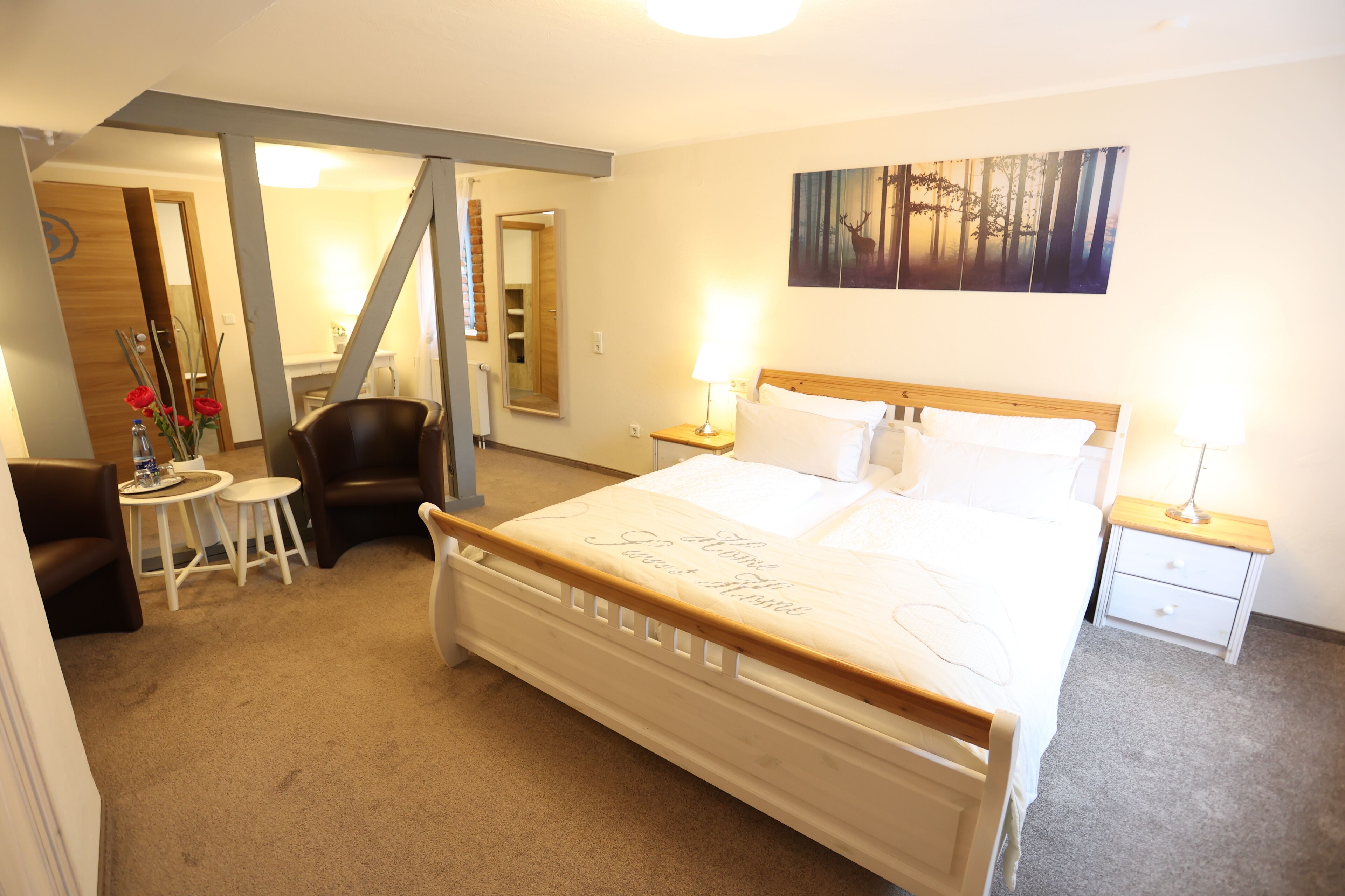 A hotel room with a large bed, two bedside tables, a chair, a small table with a vase of flowers, and a painting on the wall.