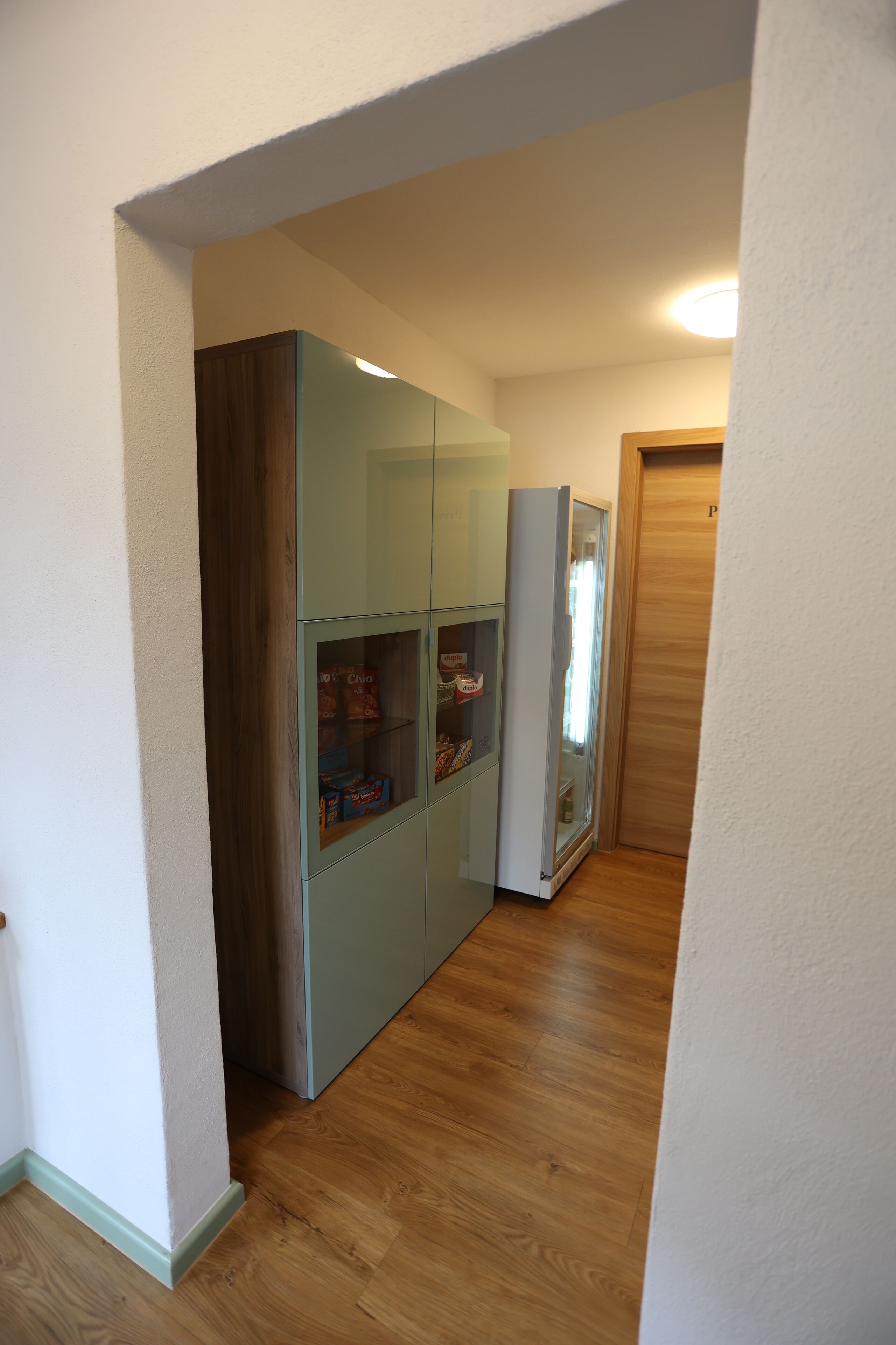 A hallway with a wooden floor, a glass-fronted cabinet, and a refrigerator.