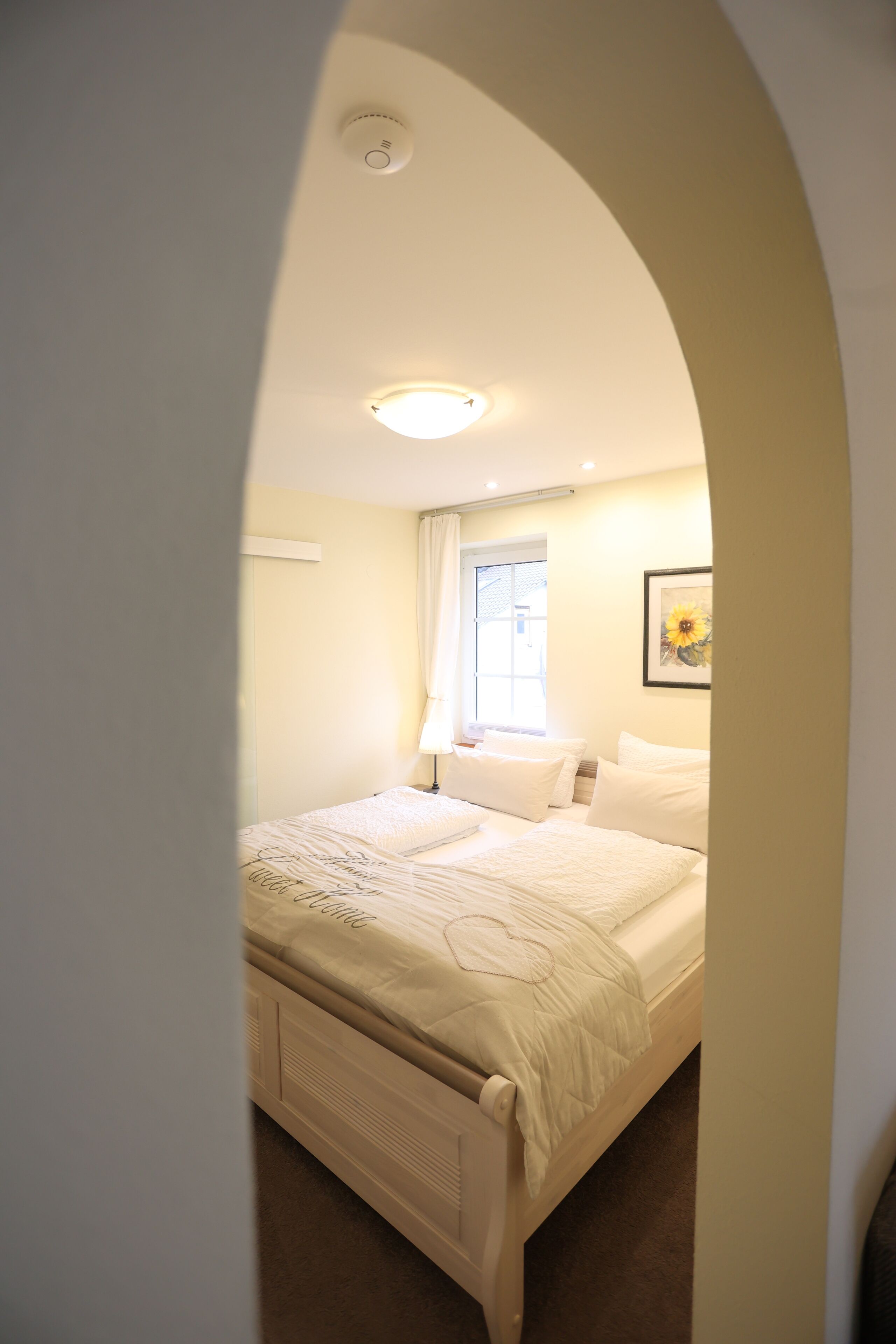 A bedroom with a bed, a window with curtains, a ceiling light, and a framed picture on the wall.