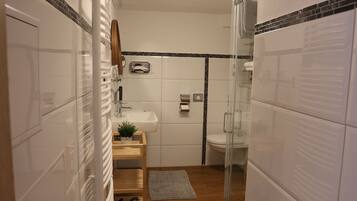 Un baño moderno con ducha de vidrio, azulejos blancos, tocador de madera y una planta pequeña.