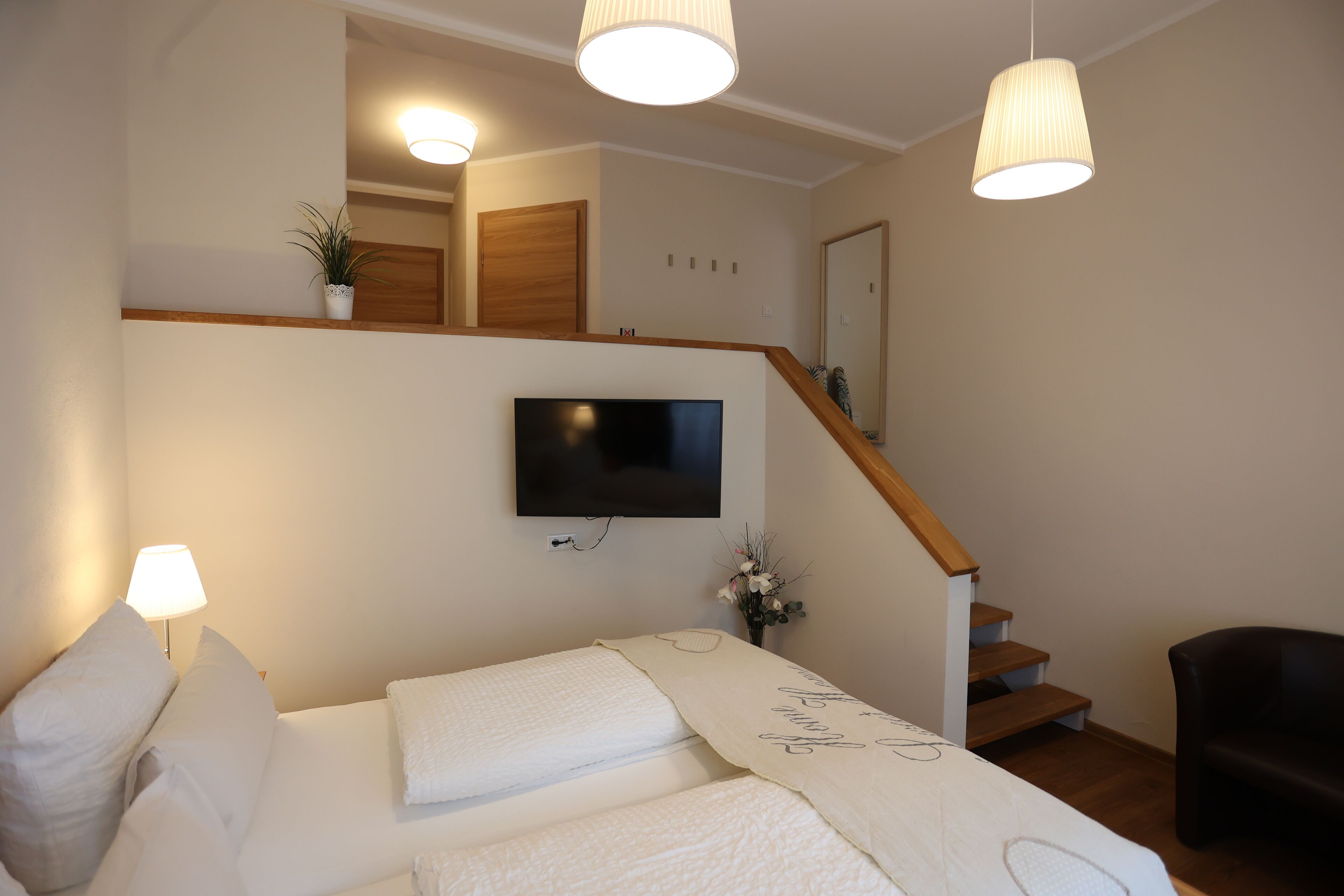 A bedroom with a bed, a TV mounted on the wall, a staircase, and a potted plant.