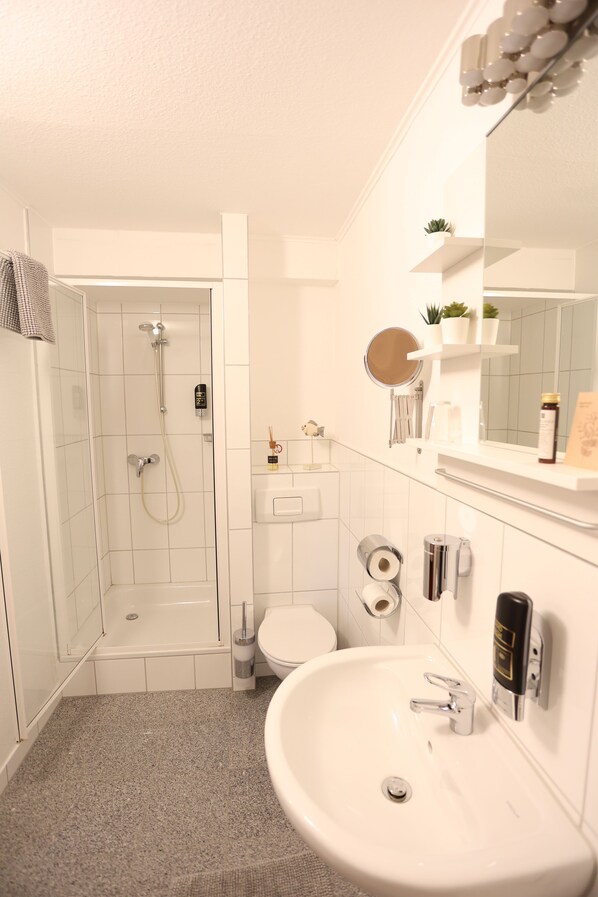 Un baño moderno con ducha, inodoro, lavabo y un espejo sobre el lavabo.