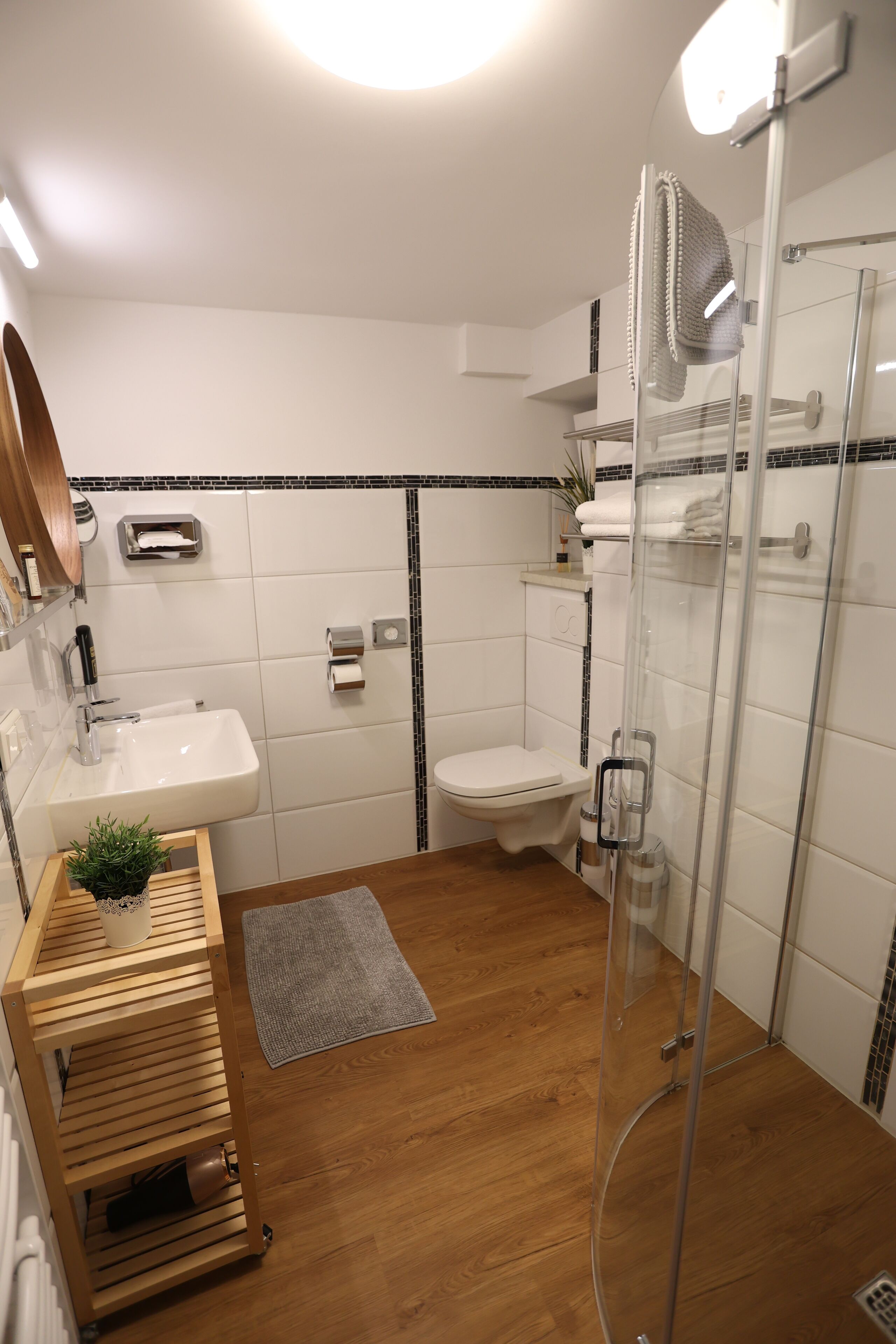 A modern bathroom with a wooden vanity, a glass shower enclosure, and a white sink.