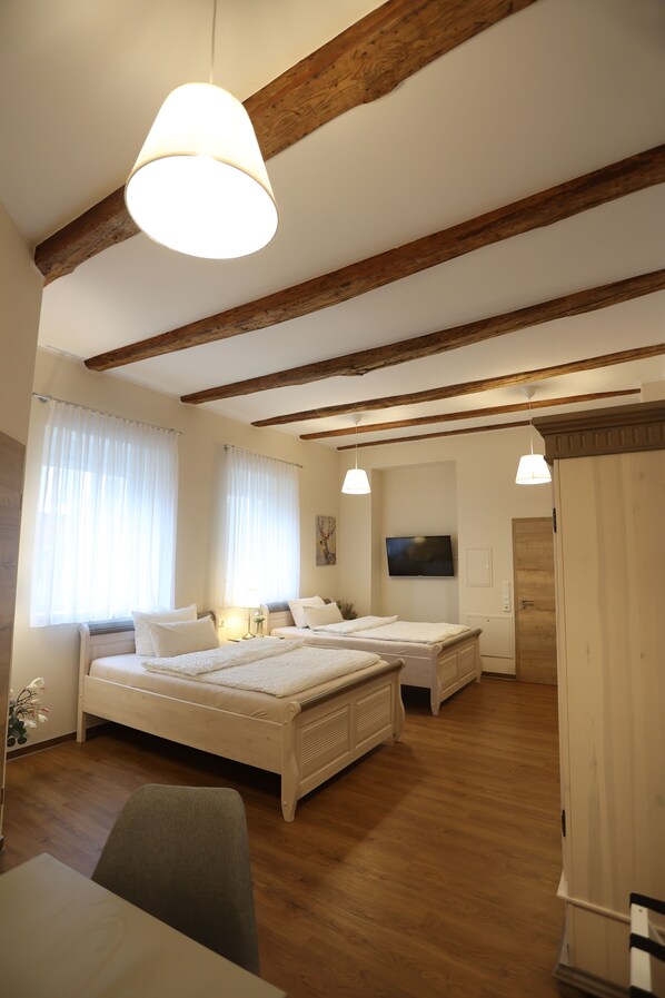 A bedroom with two beds, wooden beams, a TV, and a wardrobe. - Pension Alte Scheune (Melsungen)