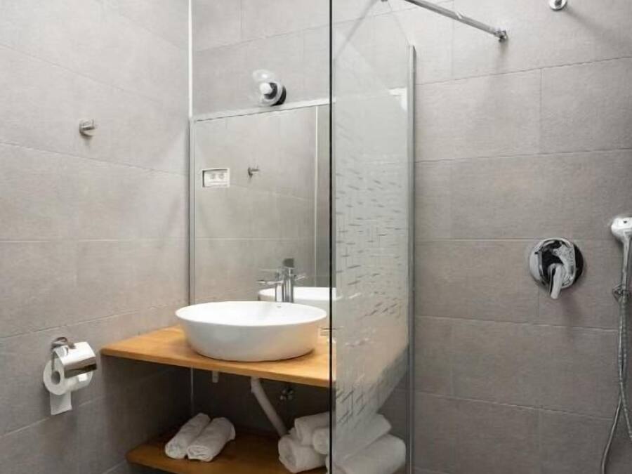 Une salle de bain moderne avec une douche à parois de verre, un lavabo blanc et une étagère en bois où sont posées des serviettes.