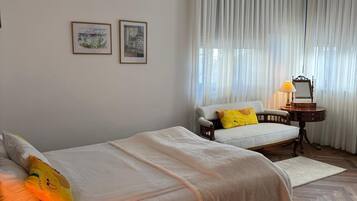 A bedroom with two beds, a bedside table with a lamp, a chair, and a small table with a lamp.