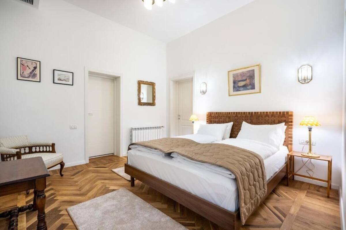 A bedroom with a wooden bed, a small table, a chair, and a radiator.