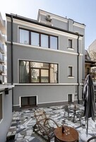 Un edificio moderno con un patio que cuenta con piso de mosaicos, mobiliario exterior y un área cubierta.