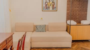 A living room with a sofa, a wooden cabinet, a framed artwork, and a herringbone-patterned floor.