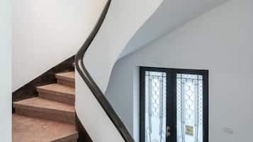 A spiral staircase with a white handrail and beige steps, leading to a door with a black frame and decorative glass panels.